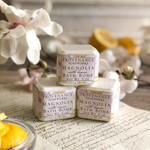 Magnolia Lemon bath bomb set on a sheet of antique paper, with magnolia blossoms and lemons in the background.